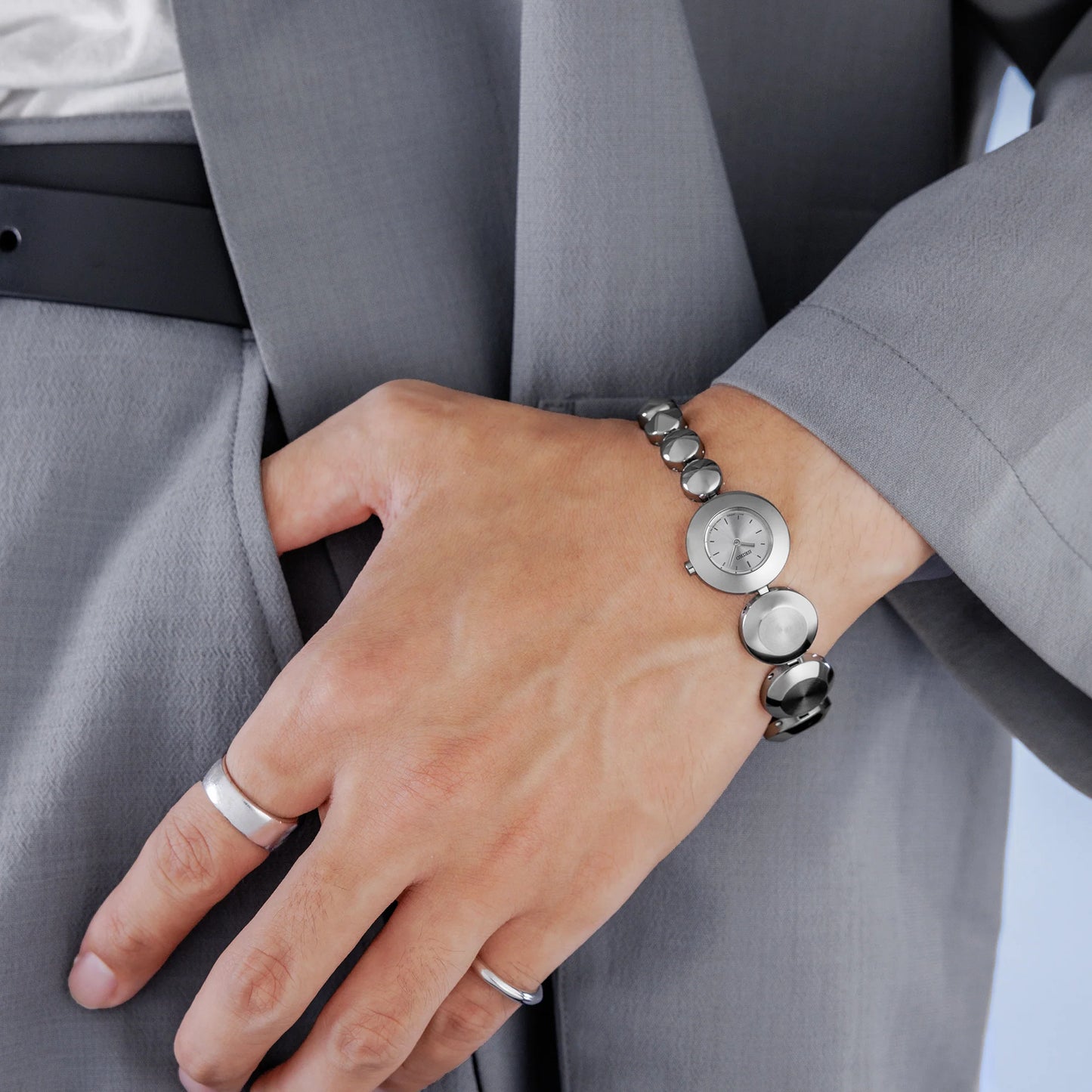 Hand wearing a bracelet with circular charms against a gray suit background