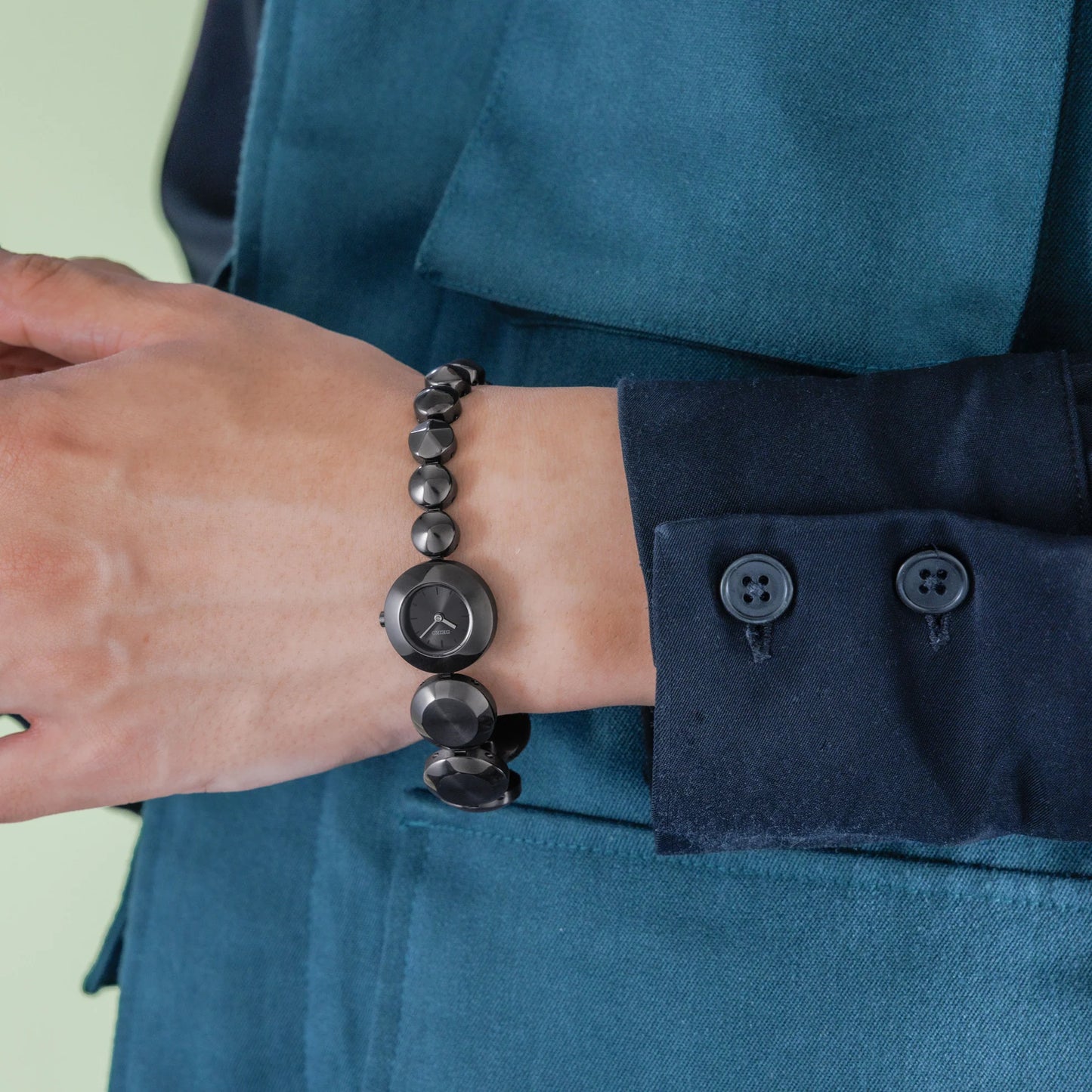 Person wearing a dark blue shirt with a bracelet on a light green background