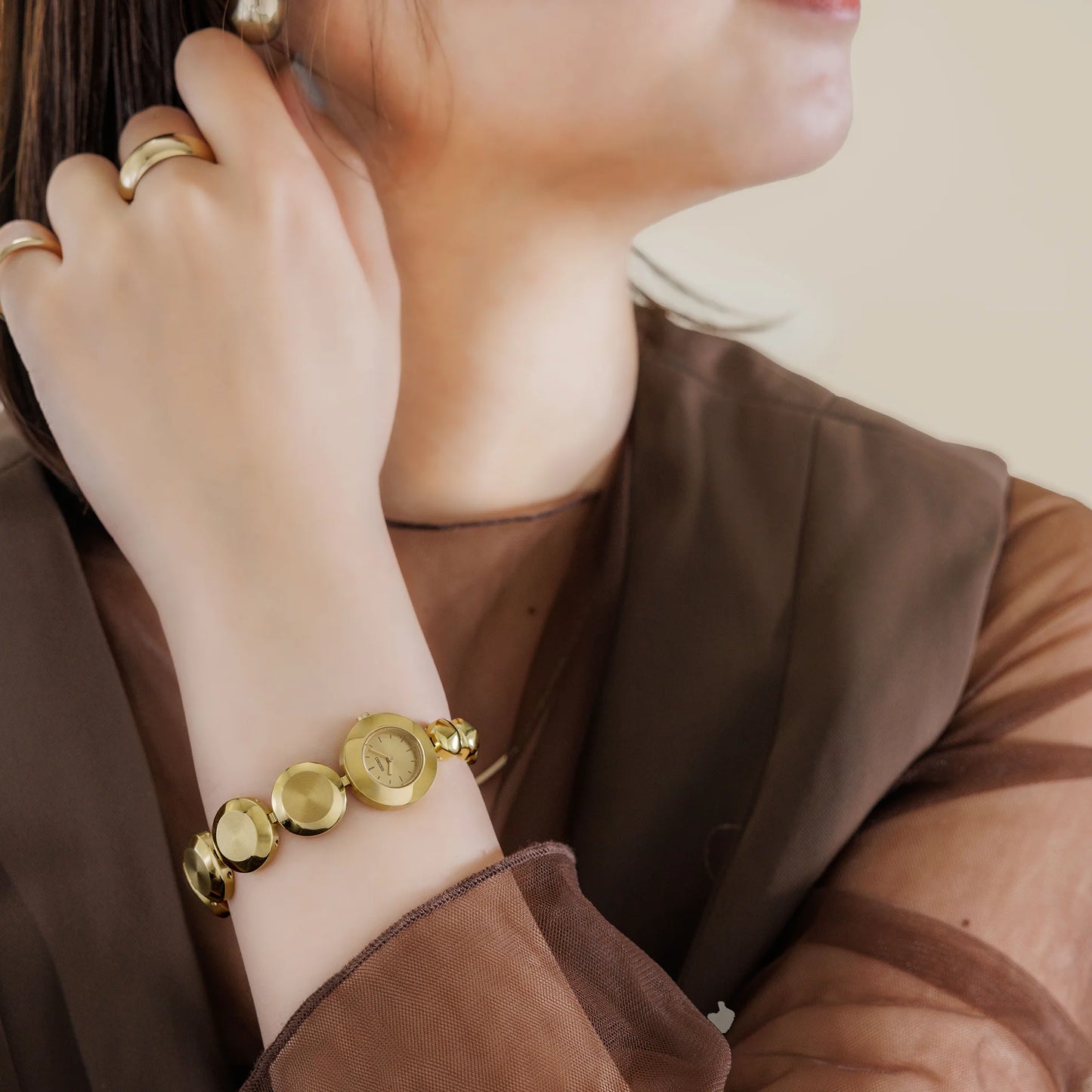 Close-up of a person wearing a gold bracelet and ring on a neutral background