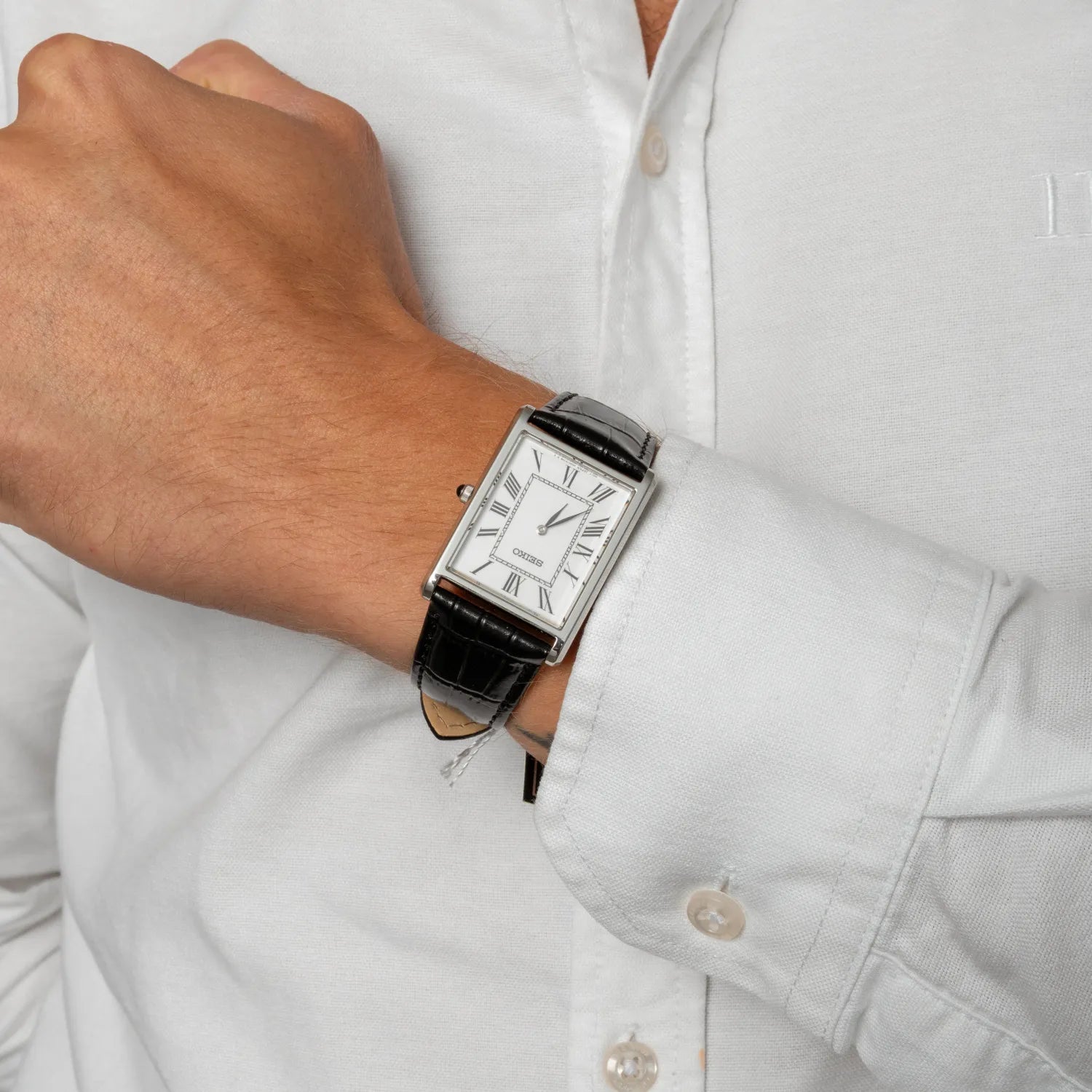 Person wearing a black wristwatch with a white face on a light background