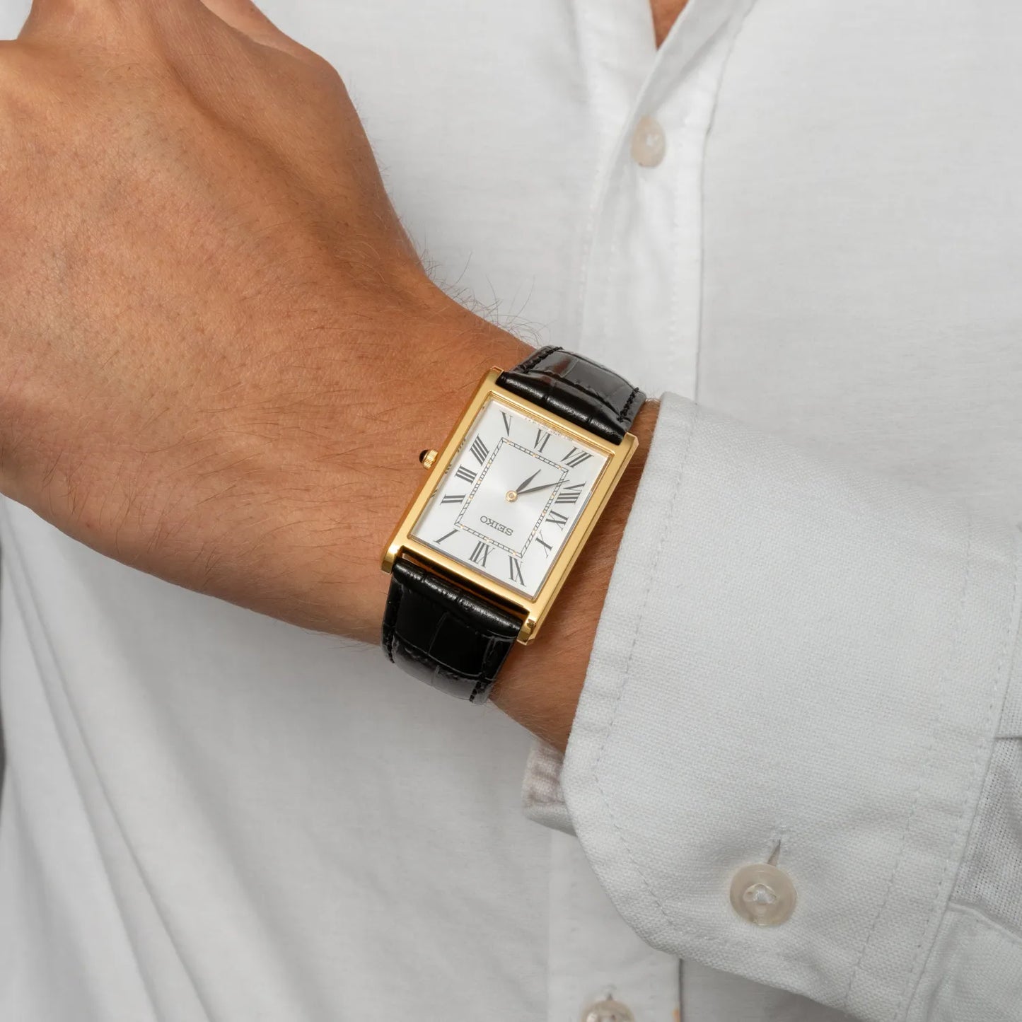 Gold watch with a black strap on a person's wrist wearing a light gray shirt.
