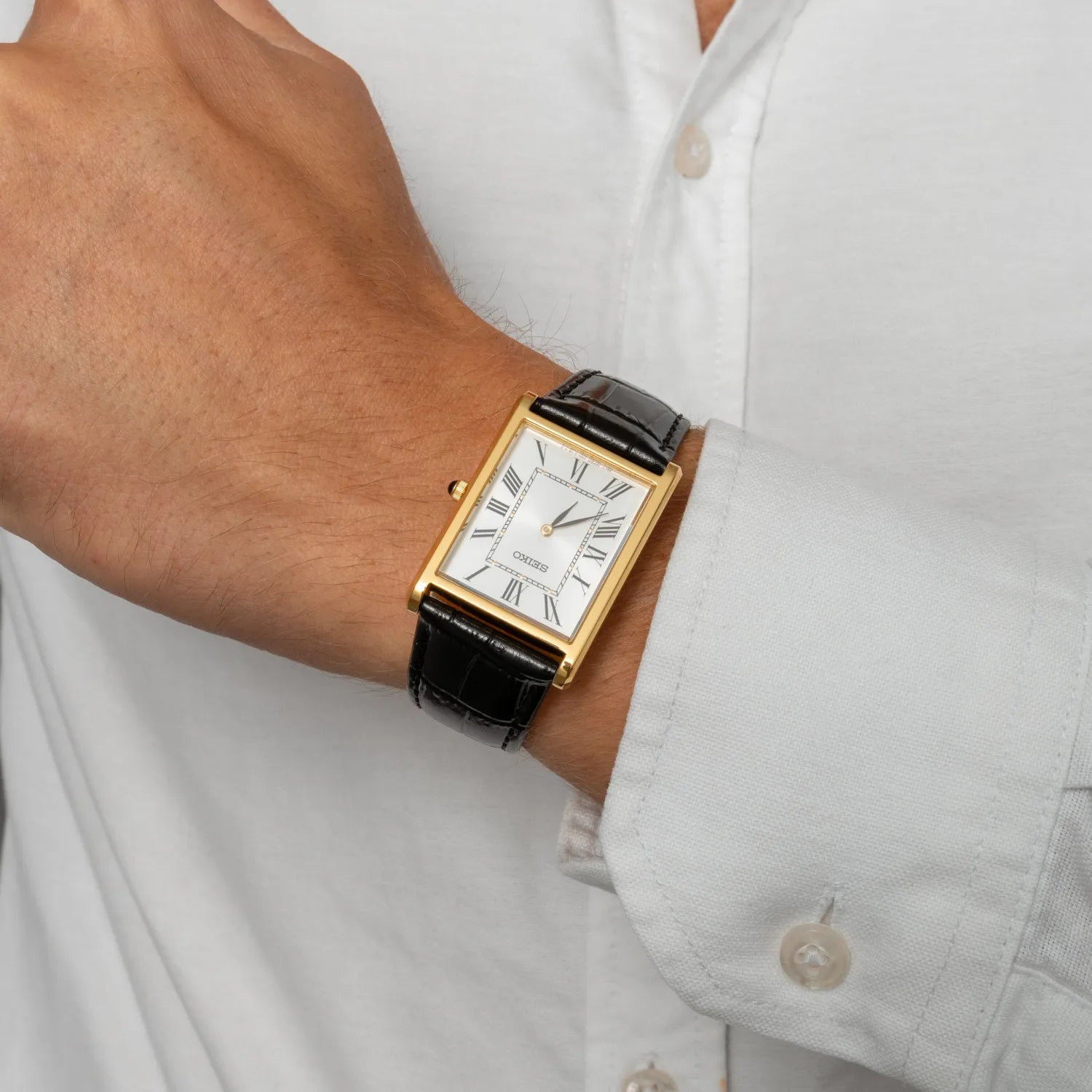 Gold watch with a black strap on a person's wrist wearing a light gray shirt.