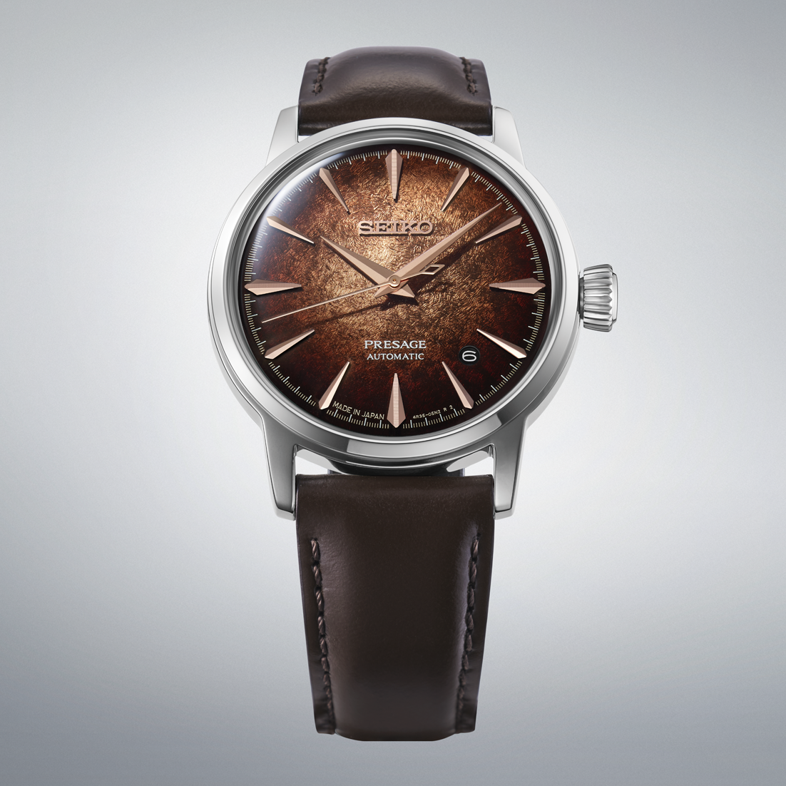 A Seiko Presage Automatic watch with a textured brown dial, rose gold-tone indices and hands, and a dark brown leather strap, shown against a neutral gray background.