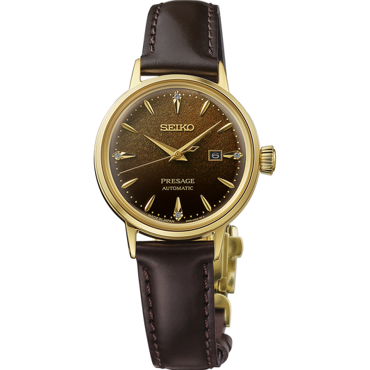 Seiko Presage Cocktail Time SRE020 women’s automatic watch inspired by the Jamaican Coffee cocktail. Features a 30.1 mm stainless steel case with gold finish, brown pressed-pattern dial with four diamond hour markers, and gold-tone hands. Comes with a dark brown leather strap, box-shaped Hardlex crystal, and date display at 3 o’clock. Powered by Caliber 2R05 automatic movement with 21 jewels, 40-hour power reserve, and manual winding. Water resistant to 50 meters.