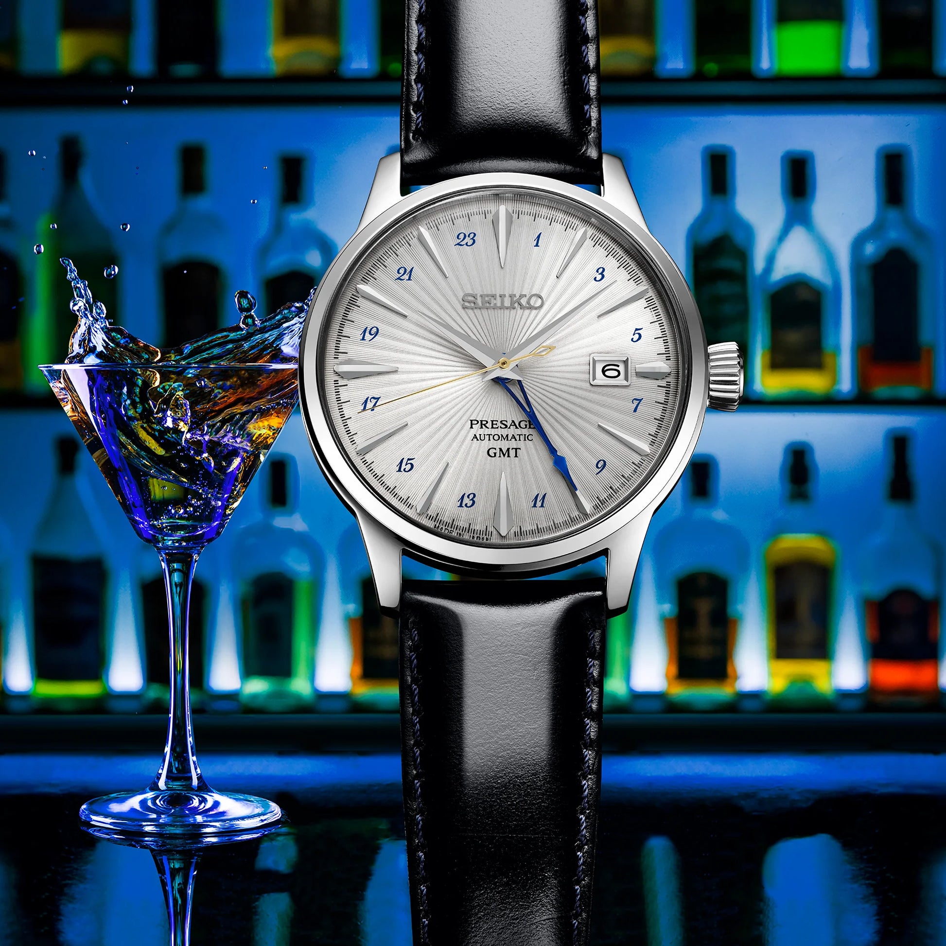 Seiko watch with a black leather strap next to a glass of water, with bottles in the background
