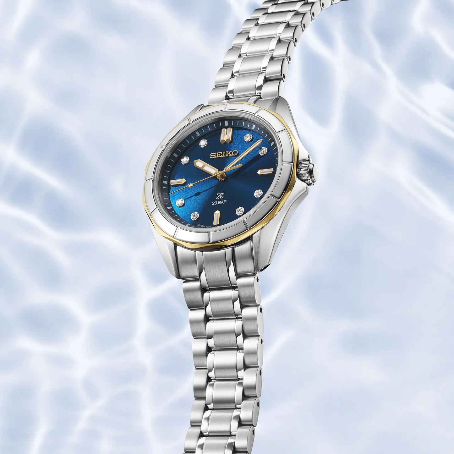 Silver Seiko watch with blue dial on a light blue water ripple background