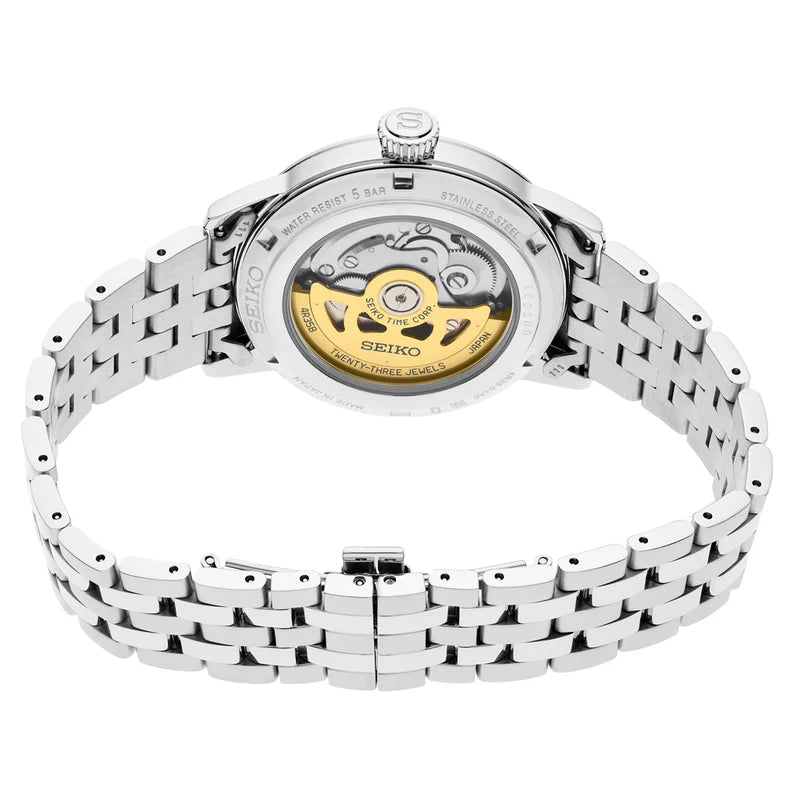 A Seiko automatic watch with a silver stainless steel link bracelet, shown from the back to reveal the transparent case and gold-tone mechanical movement.