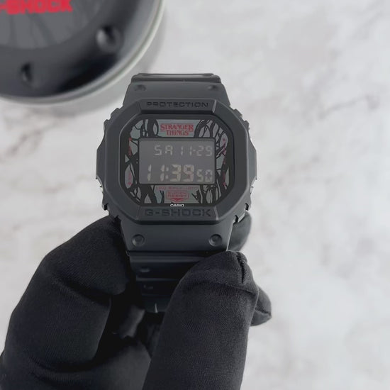 G-SHOCK DW5600STT-1 Stranger Things collaboration featuring vine-pattern dial inspired by Vecna, upside-down ‘A’ detail, red LED backlight, ‘011’ band loop tribute, bio-based black resin case and band, and special Demogorgon-themed packaging.