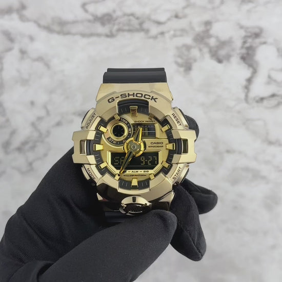 A Casio G-Shock GM700G-9A watch with a black band and gold ion-plated stainless steel bezel, featuring an analog-digital display.