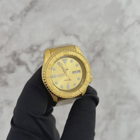 Seiko 5 Sports SRPE74 automatic watch with a metallic gold-tone dial, gold-finished stainless steel case and bracelet, unidirectional rotating bezel, and day-date display.