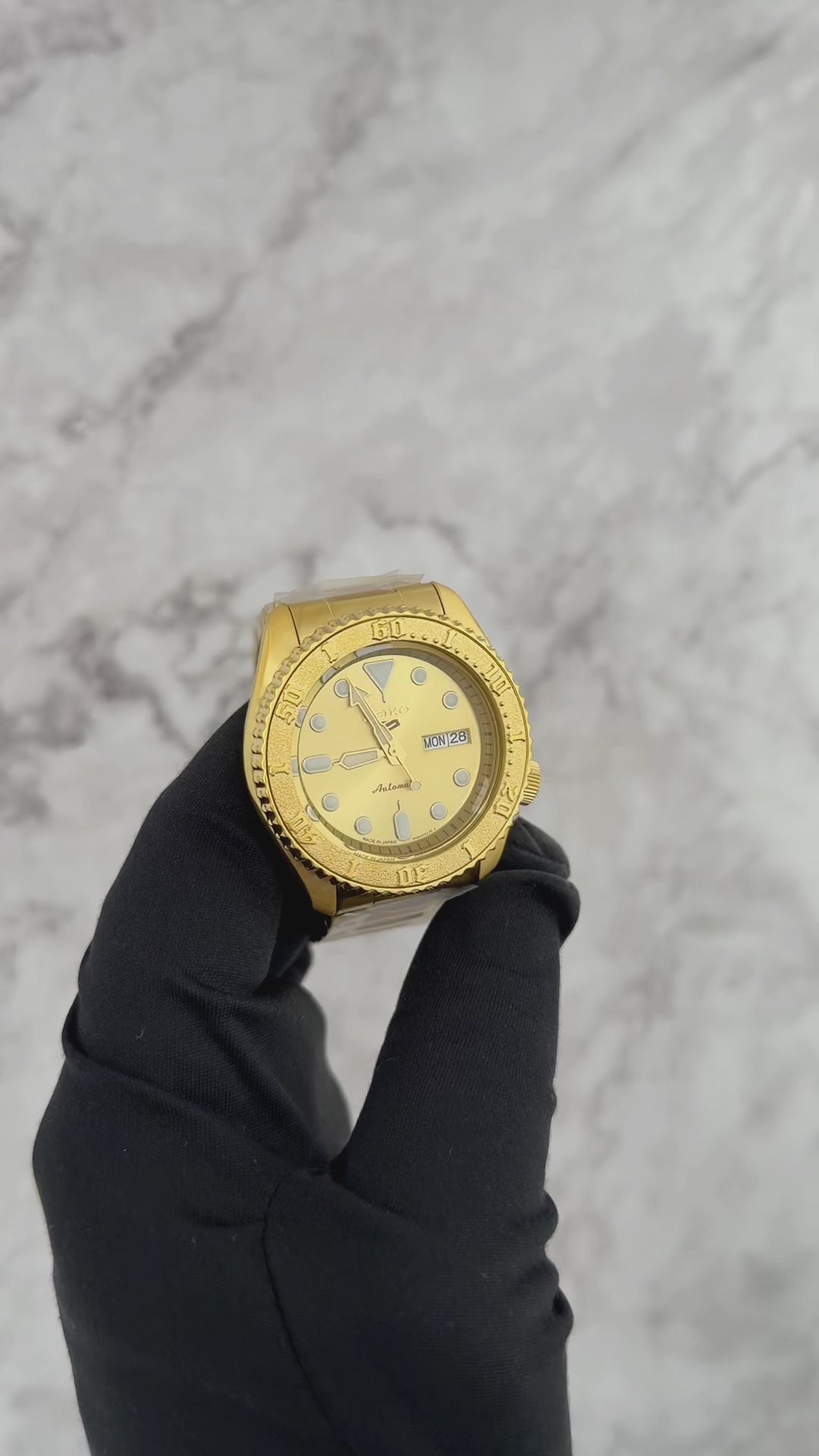 Seiko 5 Sports SRPE74 automatic watch with a metallic gold-tone dial, gold-finished stainless steel case and bracelet, unidirectional rotating bezel, and day-date display.